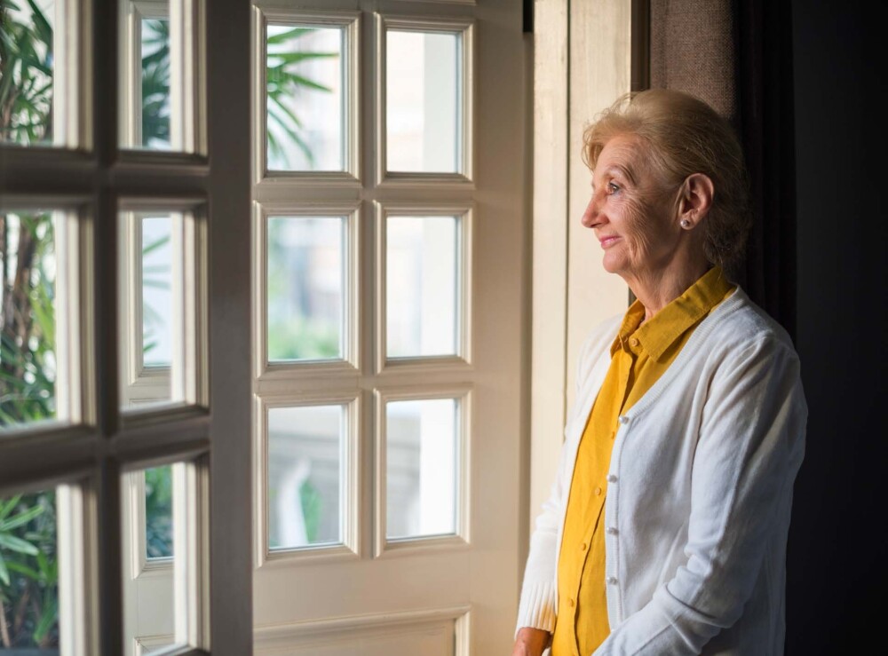 Older woman inside looking out a window