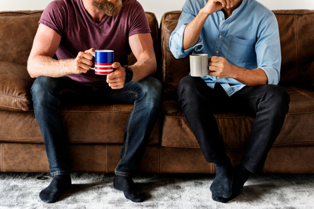 two males sitting on a couch having coffee